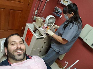 The image shows a man lying on a dental chair with a smiling expression while a dental professional attends to him.