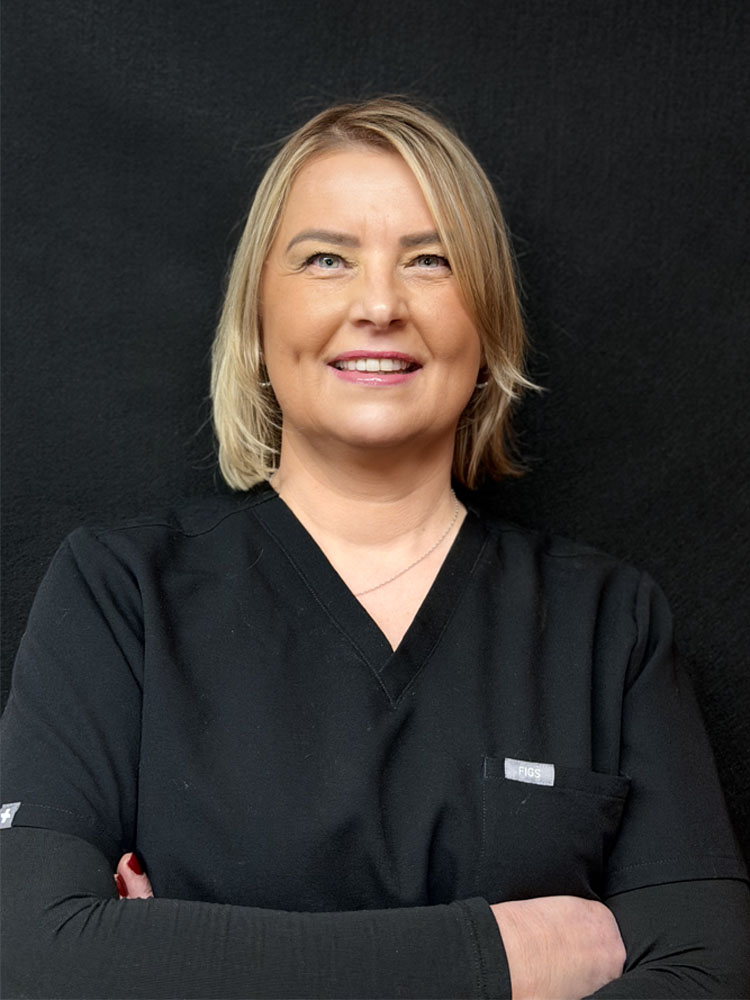 The image shows a woman wearing a white lab coat, standing with her arms crossed against a dark background.