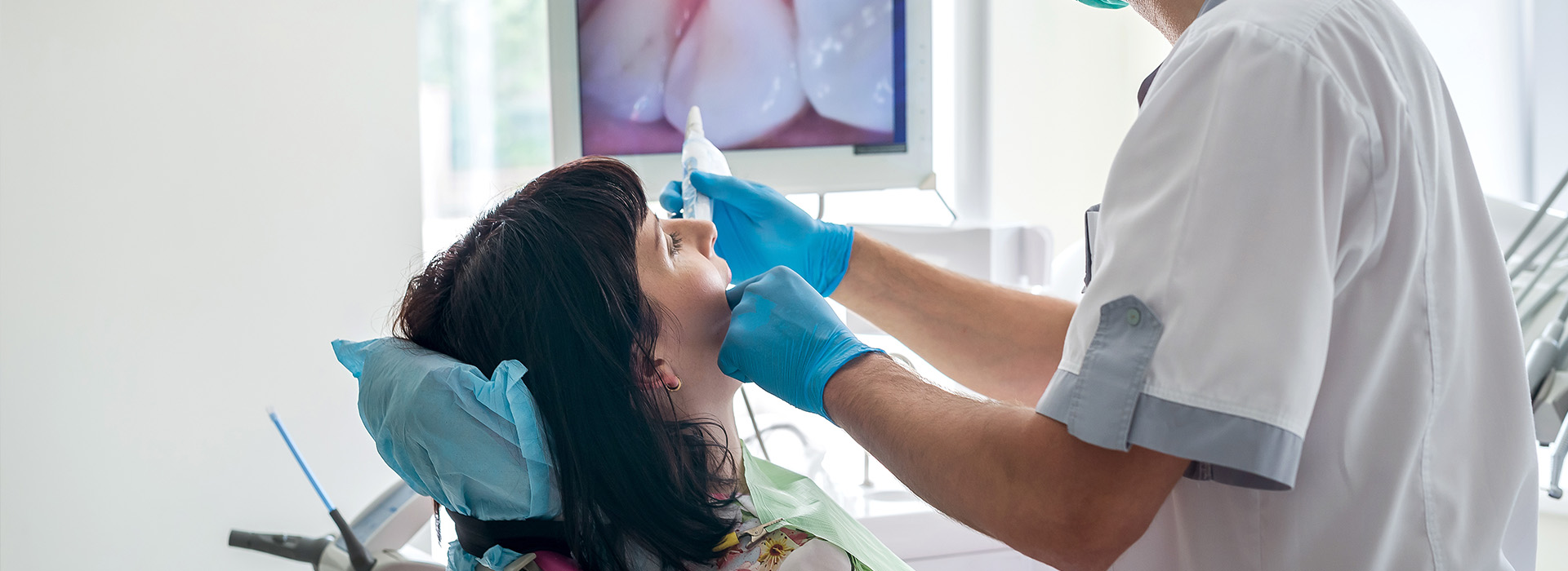 The image depicts a medical professional performing a dental procedure on a patient s mouth with the use of dental tools, while the patient is seated in a dental chair.