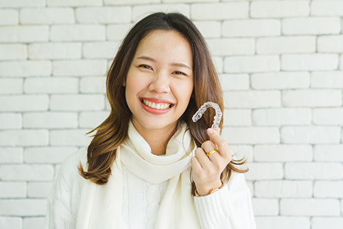 A woman holding a white letter  M  against a brick wall background.
